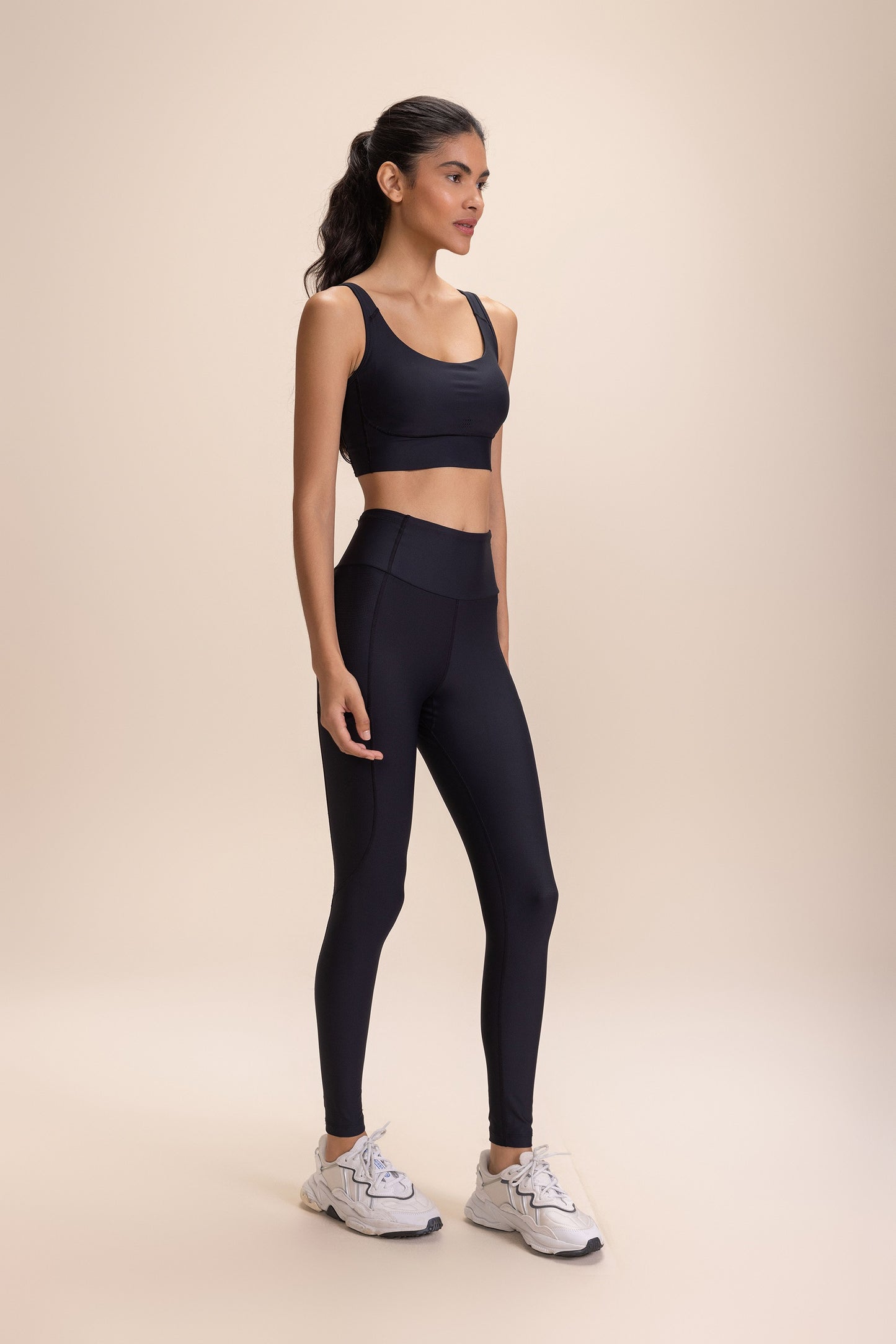 A woman wearing "Legging 6 Pockets Speed" in black, featuring high-waisted design, six pockets, paired with a matching black sports bra and white athletic shoes.