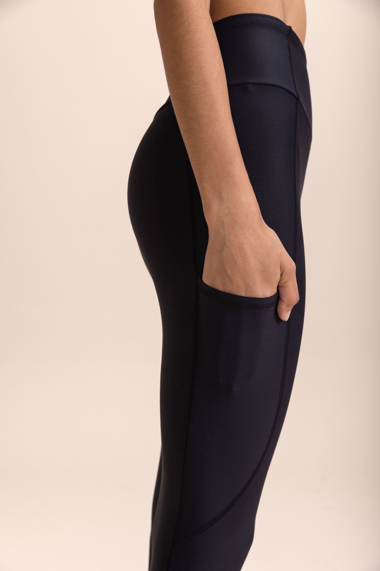 Close-up of a person wearing black leggings with a hand in one of the six pockets, highlighting the ergonomic design and high compression fabric.