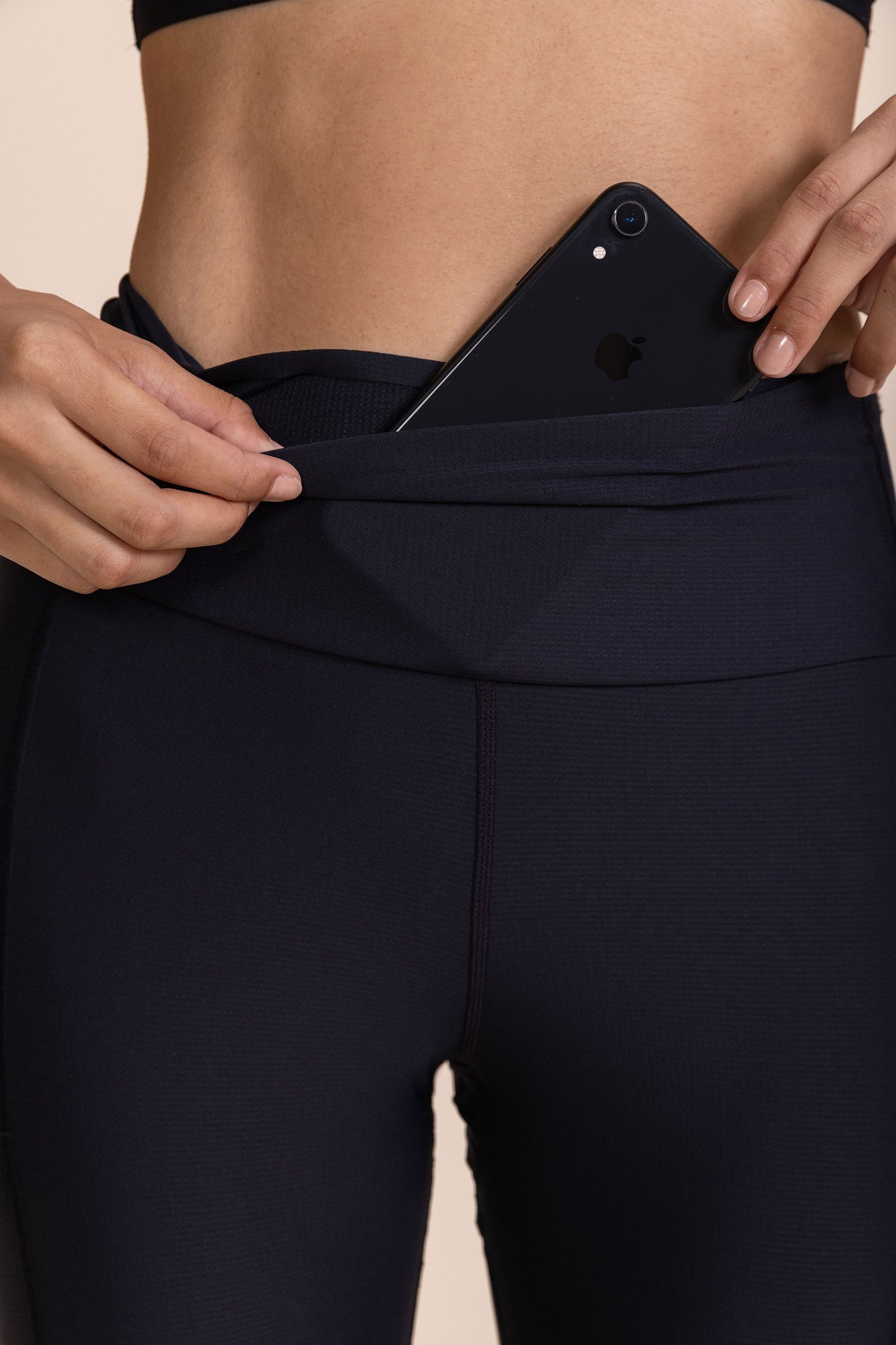 Person inserting a smartphone into a pocket on the waistband of the black "Legging 6 Pockets Speed" activewear.