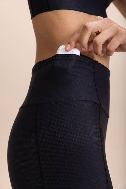 Close-up of black leggings with six pockets, showcasing a hand placing an item into one pocket.