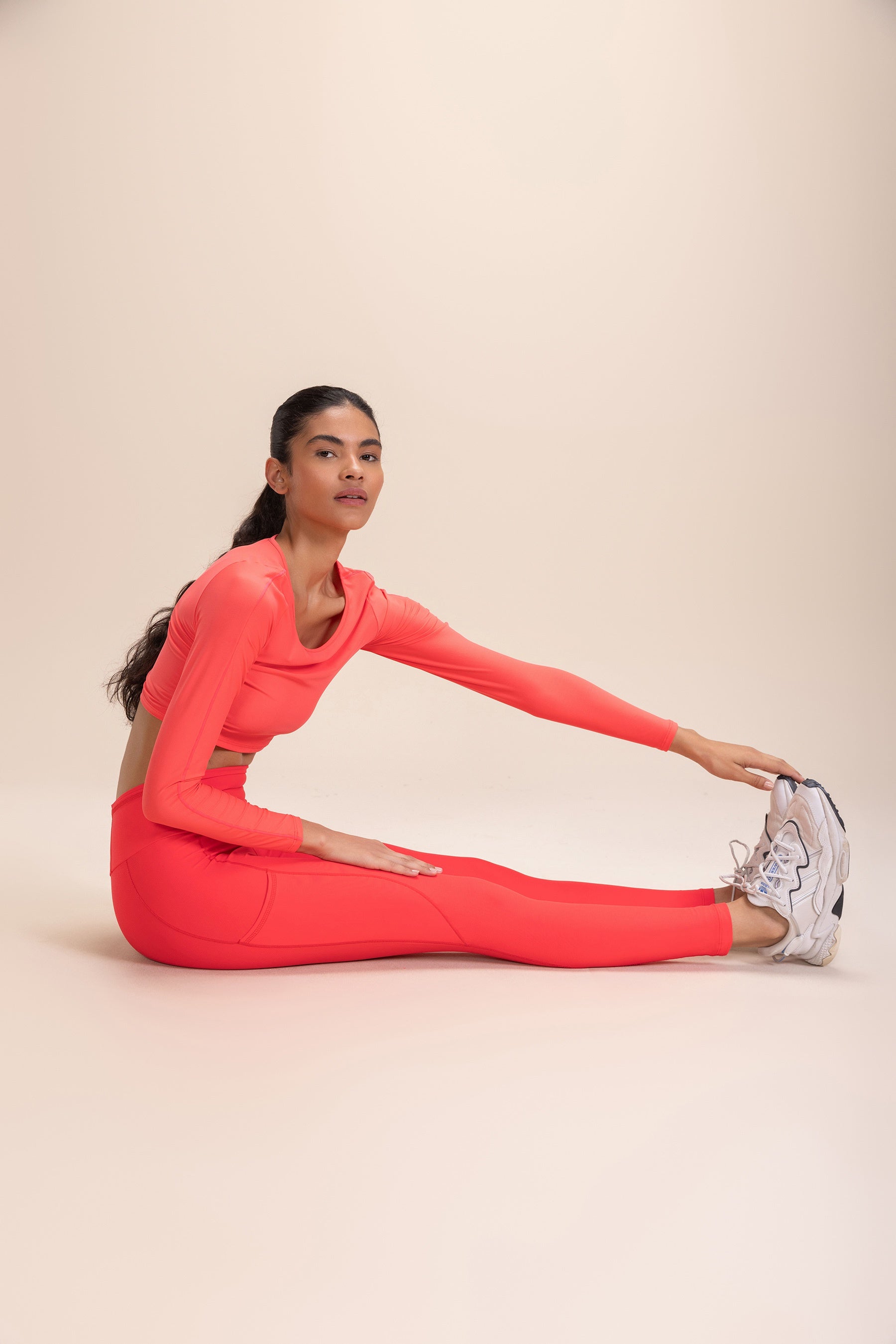 Woman wearing vibrant red Legging 6 Pockets Speed, stretching with one leg extended and holding her sneaker, showcasing the ergonomic design and high-performance fabric.