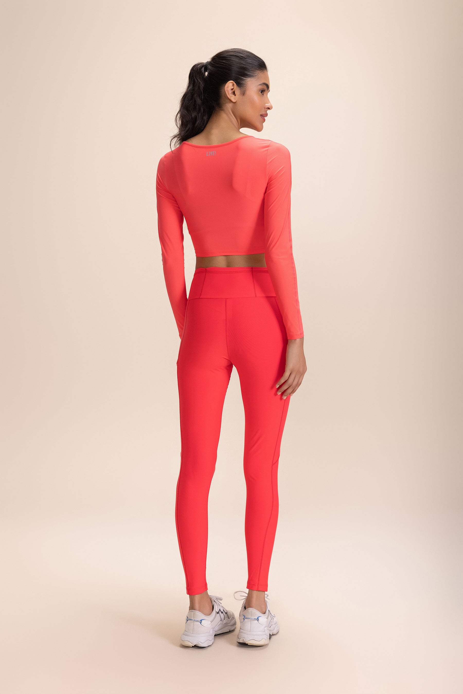 Woman wearing vivid coral athletic outfit featuring Legging 6 Pockets Speed and matching long-sleeve crop top, side view.