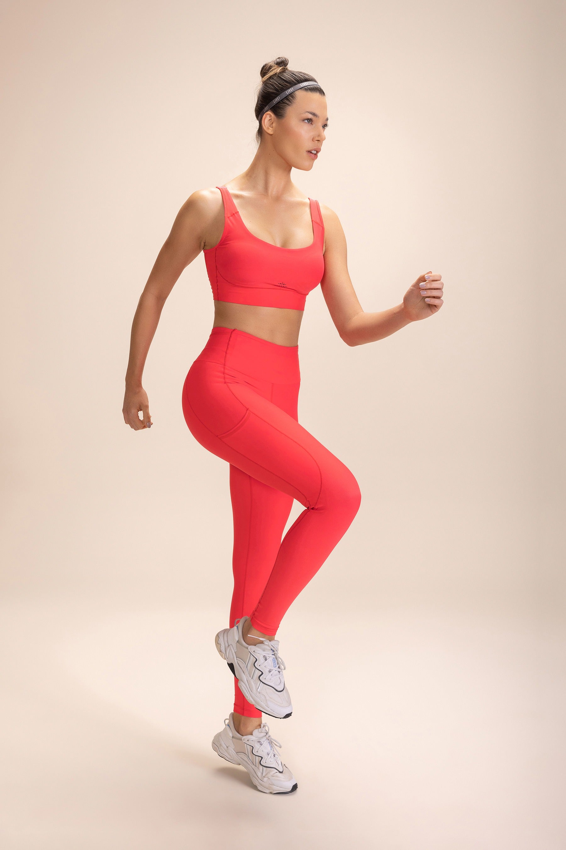 Woman wearing red "Legging 6 Pockets Speed" and matching sports bra, demonstrating a running pose against a beige background.